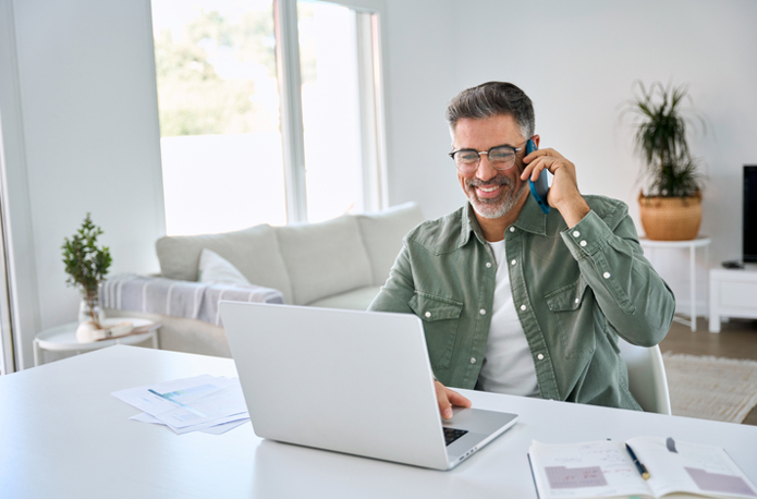 Happy middle aged entrepreneur wearing eyeglasses talking on mobile phone looking at laptop