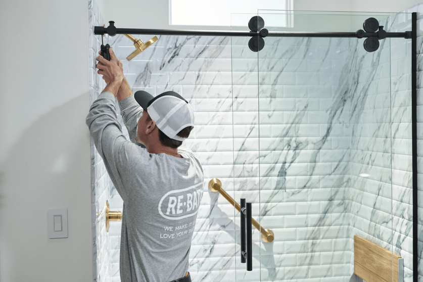 A Re-Bath employee installs a sliding glass shower door in a freshly remodeled bathroom. | Re-Bath